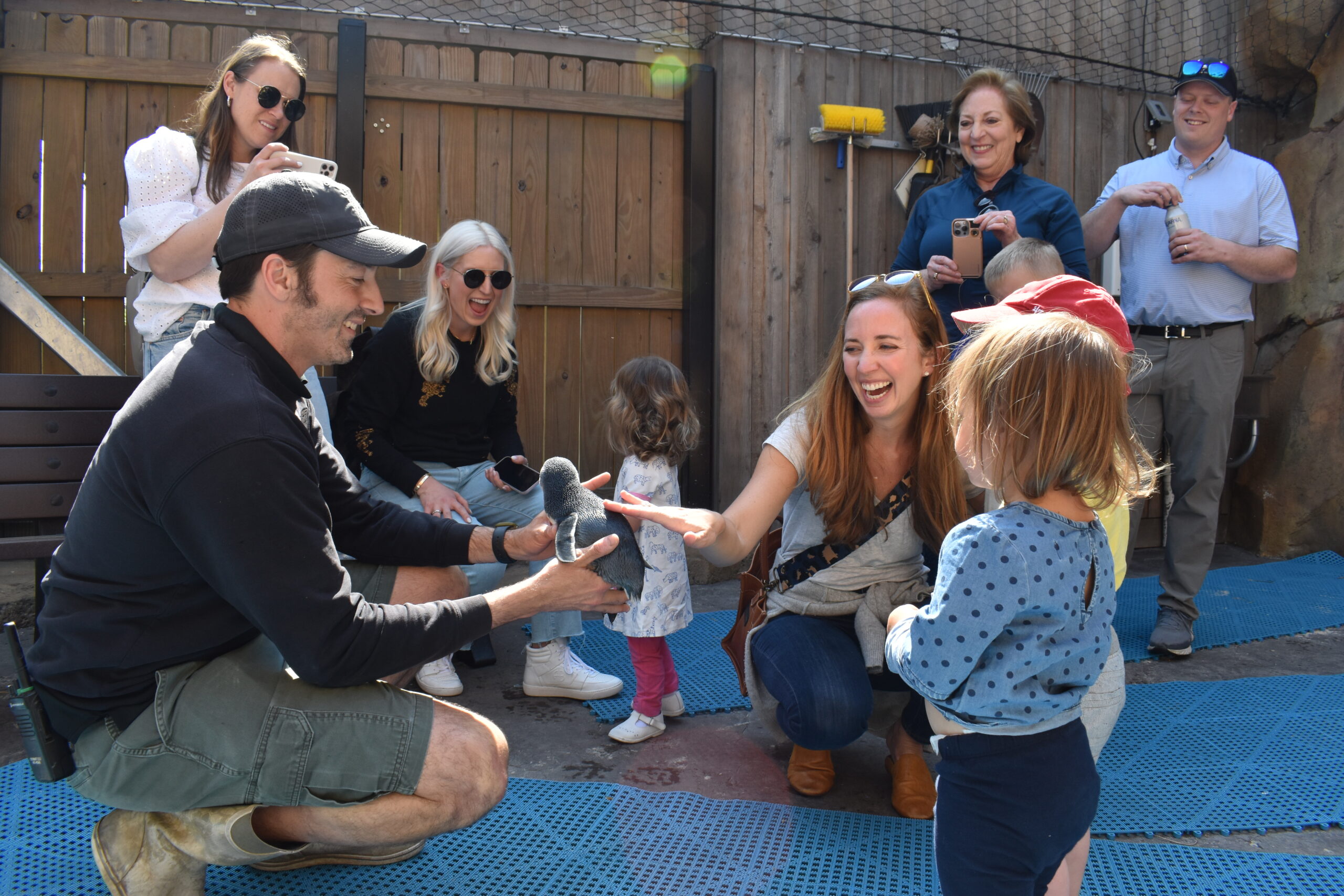 family smiling and touching a little blue penguin that a keeper is holding